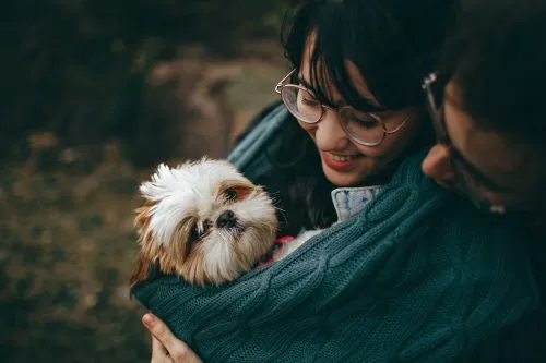 A woman holding a small dog wrapped in a green blanket outdoors.