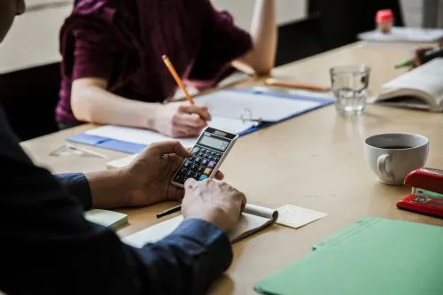 People working at a table with notebooks, a calculator, and a cup of coffee.