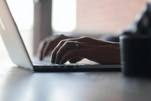 Hands typing on a laptop keyboard in a softly lit room.