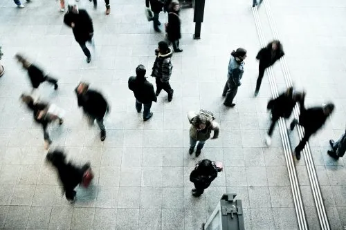 Aerial view of people walking in various directions on a gray tiled surface.