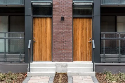 Two adjacent wooden doors on a brick building with glass balconies.