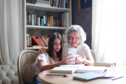 An elderly woman and a young girl take a selfie together at a table with books.