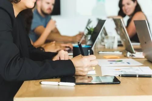 People working on laptops and documents during a meeting at a conference table.